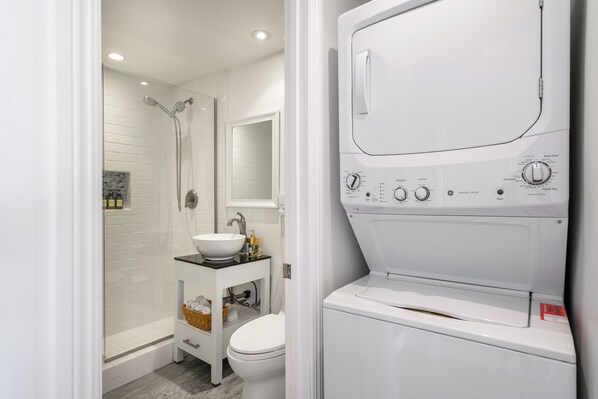 Une salle de bain moderne dotée d’un lave-linge et d’un sèche-linge intégrés, d’un lavabo blanc et d’une cabine de douche en verre.