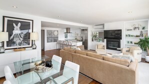 Una sala de estar moderna con una mesa de comedor de vidrio, un sofá color beige y una cocina al fondo.