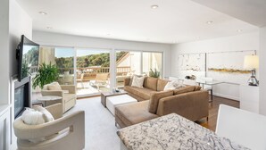 Un salón amplio con un televisor grande, asientos cómodos y vistas al exterior.