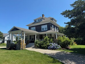 A two-story house with a covered porch and a stone wall.