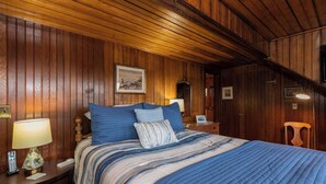 A wooden-paneled room with a bed, a nightstand, a lamp, and a framed picture on the wall. - Gorgeous Spacious Victorian Cape Cod Beach View Retreat (Falmouth)