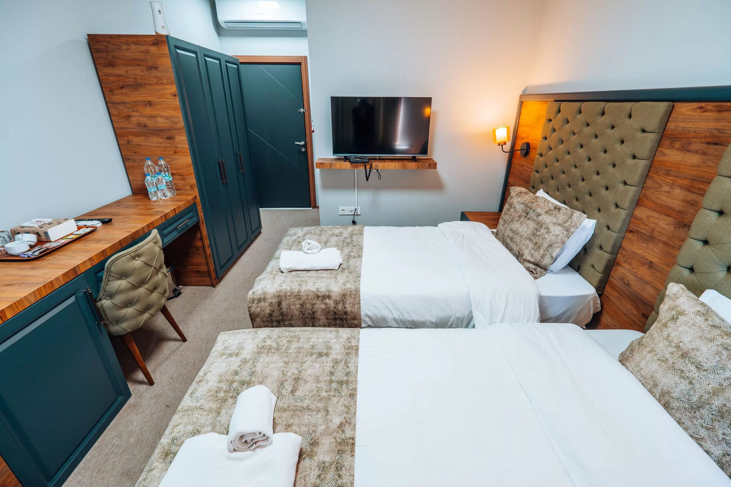 A hotel room with two beds, a desk with a chair, a TV mounted on the wall, and a wardrobe.