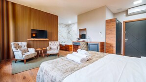 Camera d'albergo con un letto grande, due poltrone, una scrivania con uno specchio, una TV a schermo piatto montata a parete e una parete rivestita in legno.