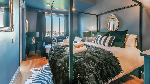 Un dormitorio moderno con cama con dosel, un espejo grande y vistas a la ciudad a través de la ventana.