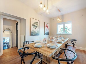 A dining area with a long wooden table set for six, black chairs, and hanging light fixtures.