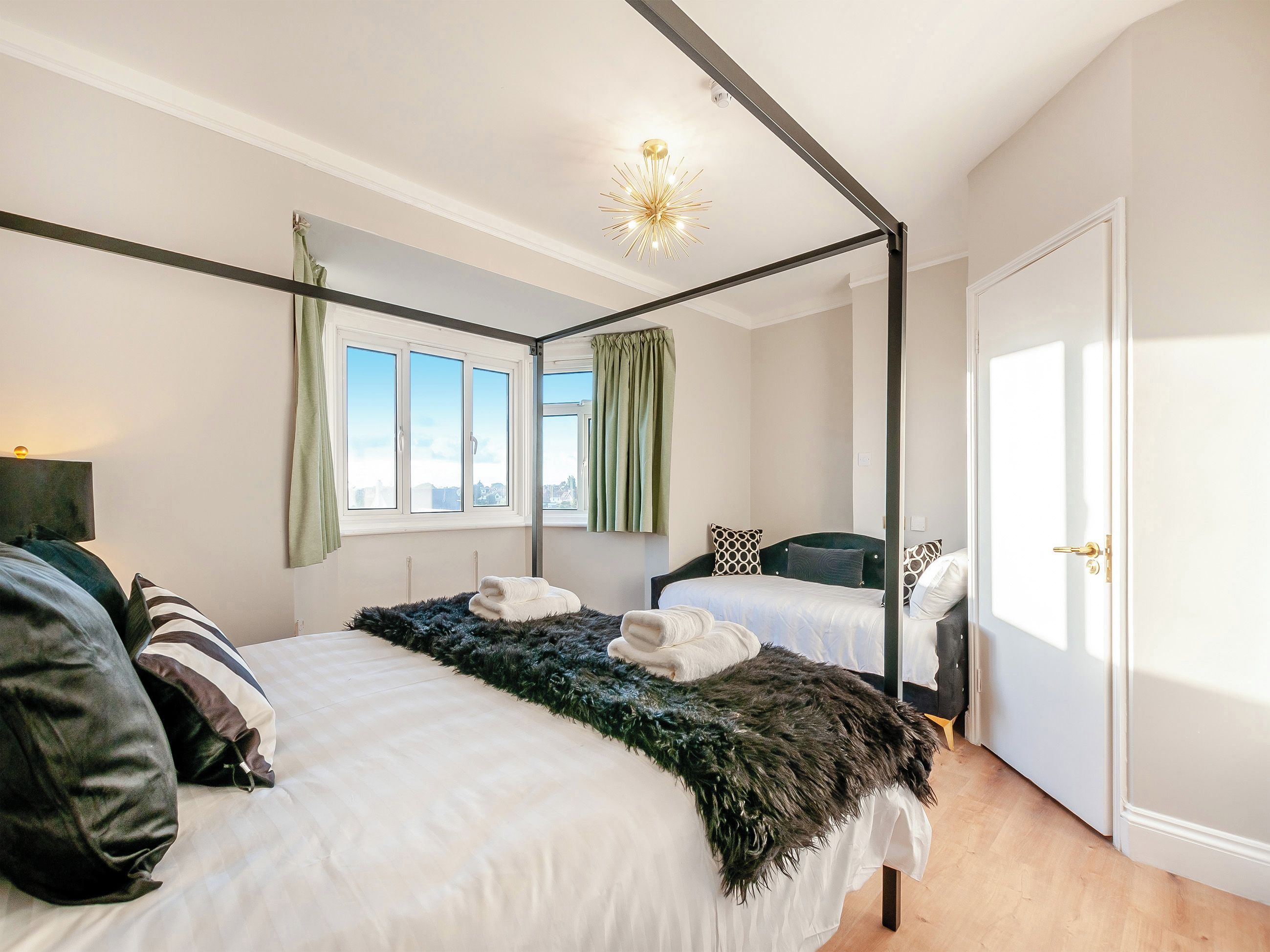 A modern bedroom with a four-poster bed, a second bed, a large window, and a door.