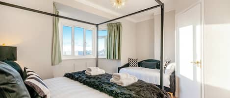 A modern bedroom with a four-poster bed, a second bed, a large window, and a door.