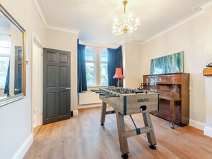 A room with a wooden floor, a foosball table, a piano, and a chandelier.