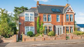 A two-story brick house with a sloped roof, multiple windows, and a small garden area.