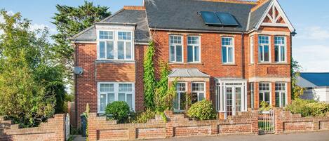 A two-story brick house with a sloped roof, multiple windows, and a small garden area.