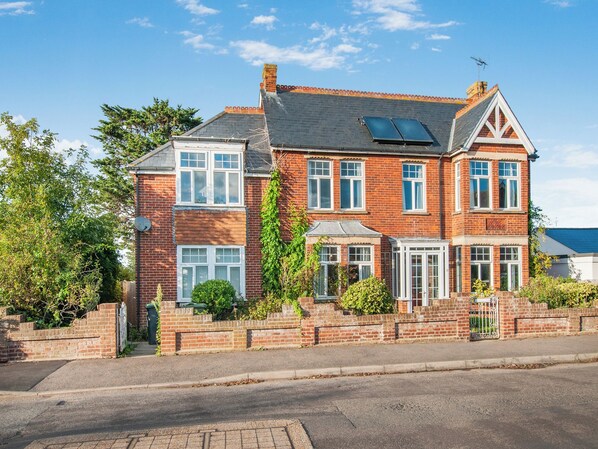 A two-story brick house with a sloped roof, multiple windows, and a small garden area.