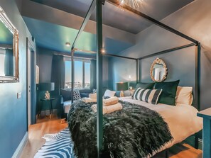 A modern bedroom with a four-poster bed, a large mirror, and a view of the city through the window.