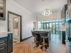 A modern kitchen with a central island, bar stools, and a view through large windows.