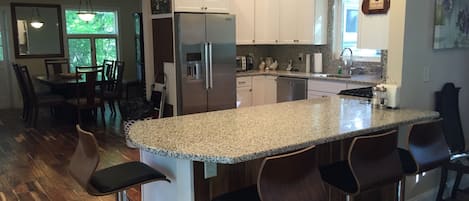 A modern kitchen with a granite countertop, stainless steel appliances, and a dining area with wooden chairs.