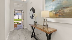 A hallway with a wooden console table, a round mirror, and a painting on the wall. - Luxury 6BR Escape – Pool, Water Slides & Lazy River Near Disney! (Four Corners)