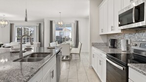 A modern kitchen with granite countertops, stainless steel appliances, and white cabinetry. - Luxury 6BR Escape – Pool, Water Slides & Lazy River Near Disney! (Four Corners)