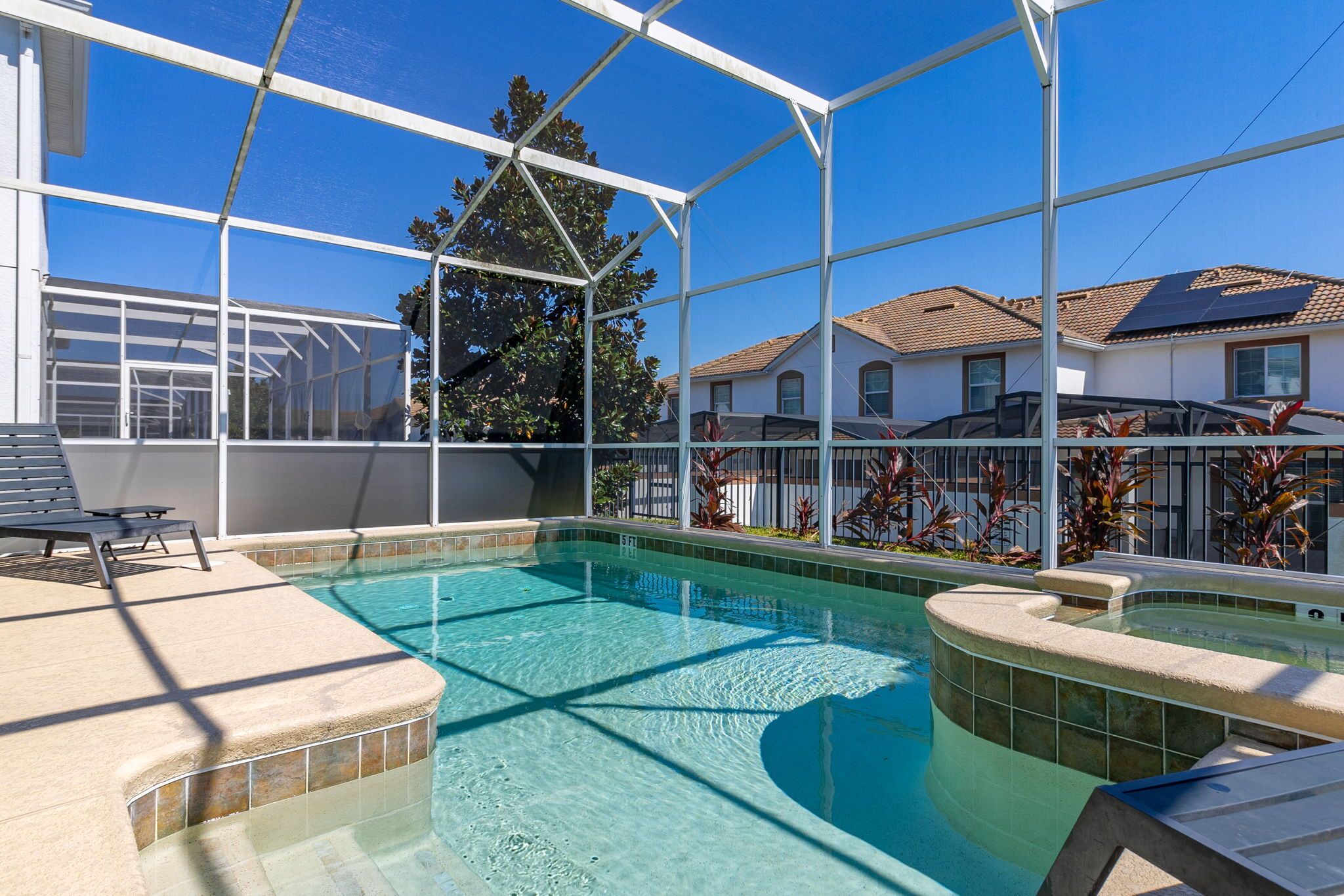 A swimming pool with a glass enclosure, a lounge area with a chair, and a view of houses in the background.
