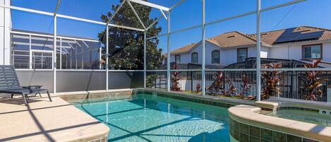 A swimming pool with a glass enclosure, a lounge area with a chair, and a view of houses in the background.