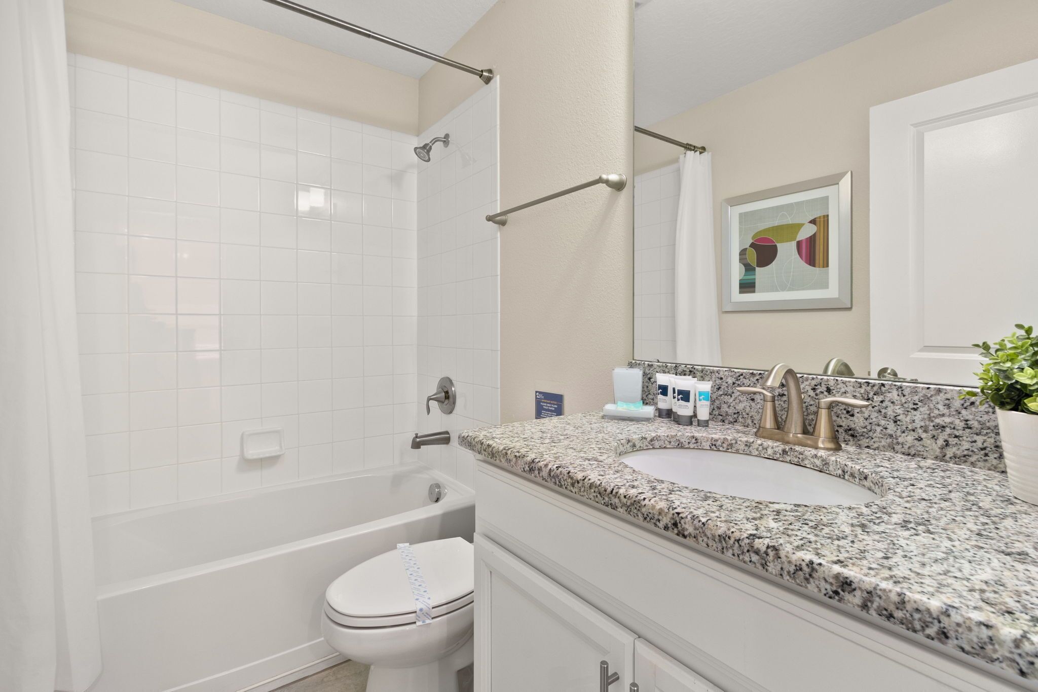 Un baño con inodoro blanco, bañera y lavamanos de granito con espejo arriba.