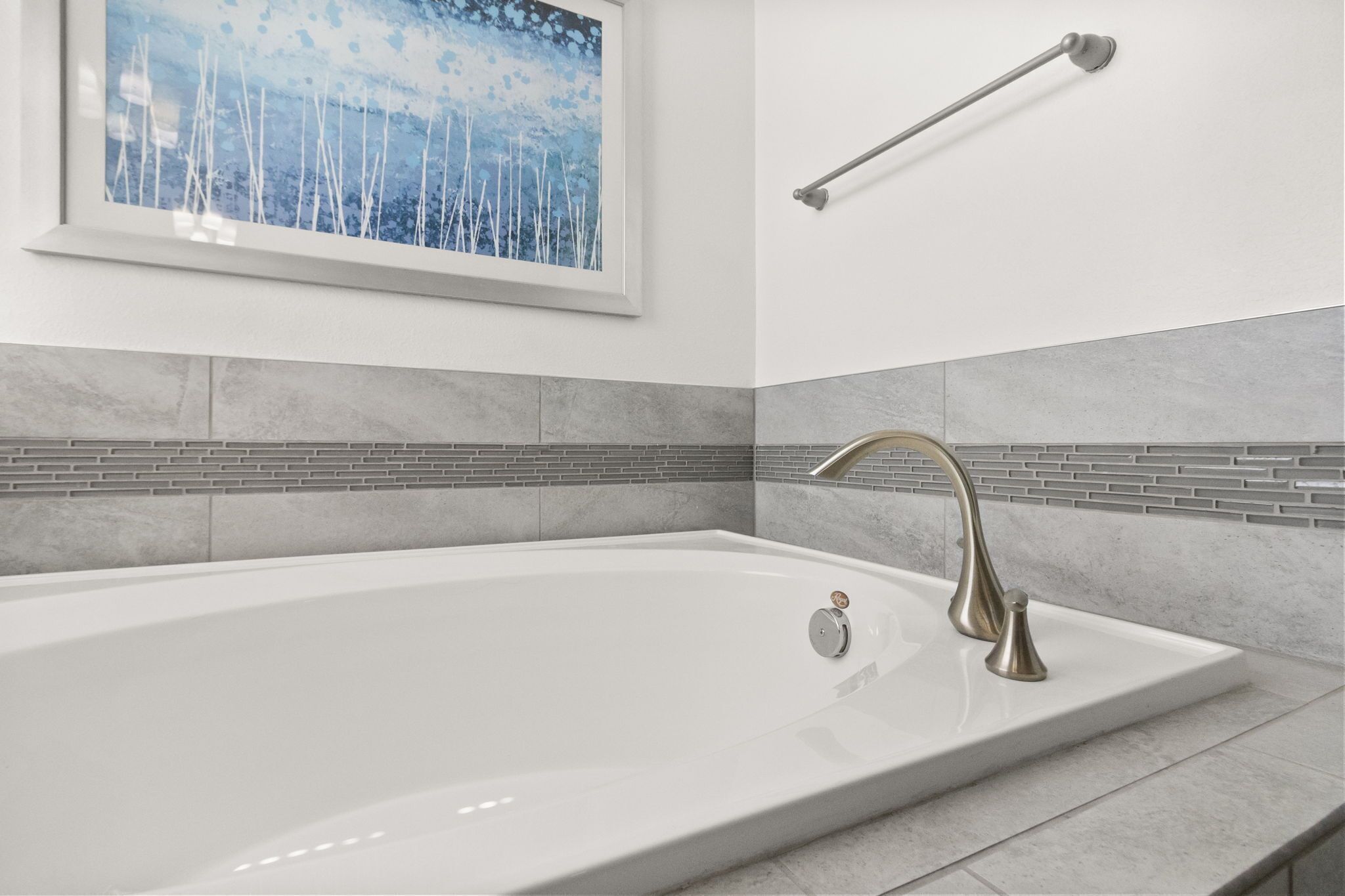 Une salle de bain moderne avec une grande baignoire, une œuvre d’art encadrée au-dessus de la baignoire et un porte-serviettes.