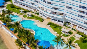 A hotel with a large swimming pool surrounded by palm trees and sun loungers. - Beautiful 2-bedroom condo in fabulous Guayacanes with WiFi, AC (Guayacanes)
