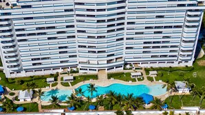 A high-rise hotel with multiple balconies, a central swimming pool, and a beachfront. - Beautiful 2-bedroom condo in fabulous Guayacanes with WiFi, AC (Guayacanes)