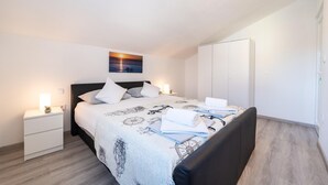 Quarto bem arrumado com cama, mesas de cabeceira, guarda-roupa e um quadro na parede.