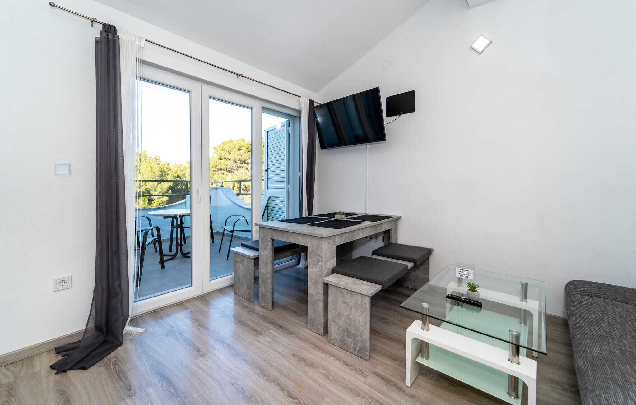 Una sala de estar moderna con una mesa de centro de vidrio, un televisor de pantalla plana montado en la pared y un ventanal corredero que da a un espacio exterior.