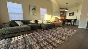 A living room with a sectional sofa, a dining area with a table and chairs, and a kitchen in the background.