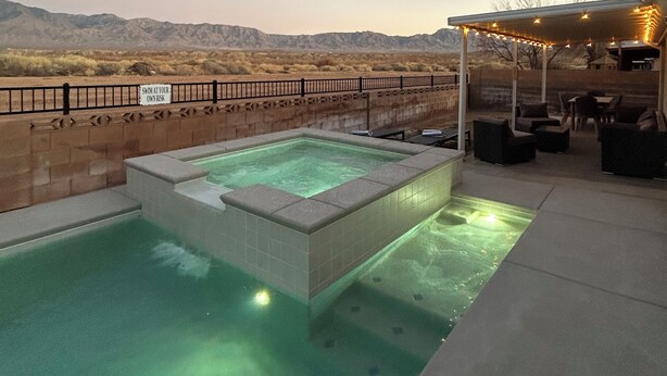 A hot tub with a view of mountains, a fenced patio area, and outdoor seating.