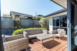 Una terraza de madera con mobiliario de mimbre, que incluye un sofá, sillas y una mesa de vidrio.