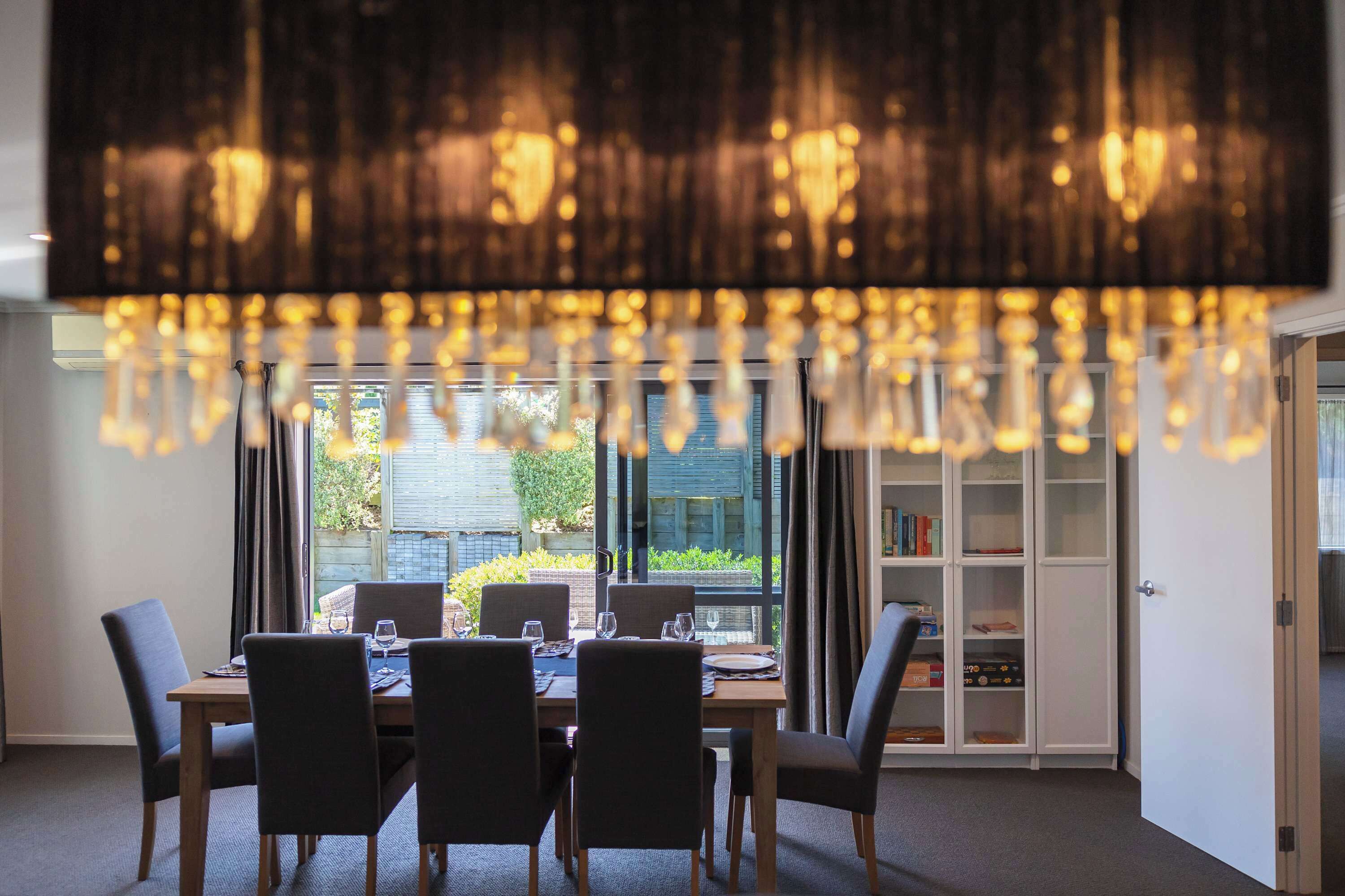 A dining area with a table set for four, a bookshelf, and a view of greenery outside.