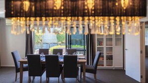 A dining area with a table set for four, a bookshelf, and a view of greenery outside. - Forest Lakes Lux - Spa Pool, Ride to Forest (Rotorua)