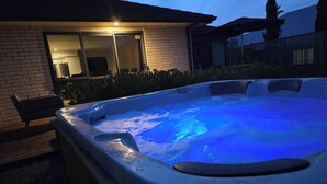 A hot tub with a blue light, surrounded by a brick house and a wooden bench. - Forest Lakes Lux - Spa Pool, Ride to Forest (Rotorua)