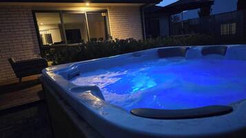 A hot tub with a blue light, surrounded by a brick house and a wooden bench.