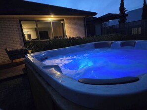 A hot tub with a blue light, surrounded by a brick house and a wooden bench.