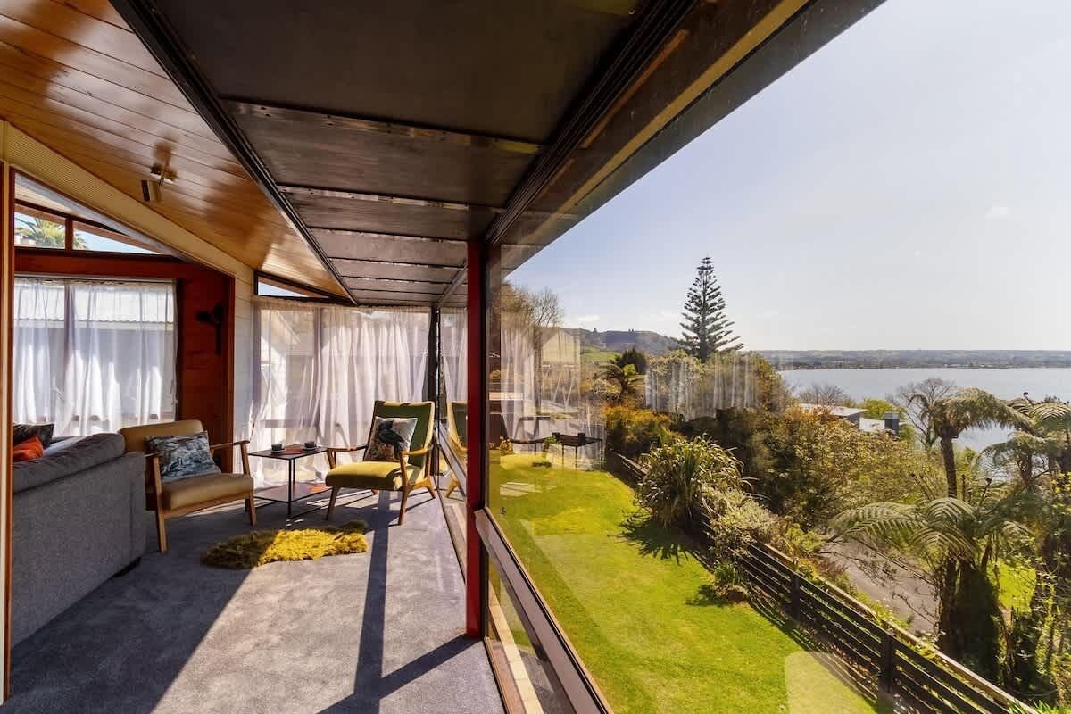 A modern living room with a large window overlooking a lush garden and a body of water.