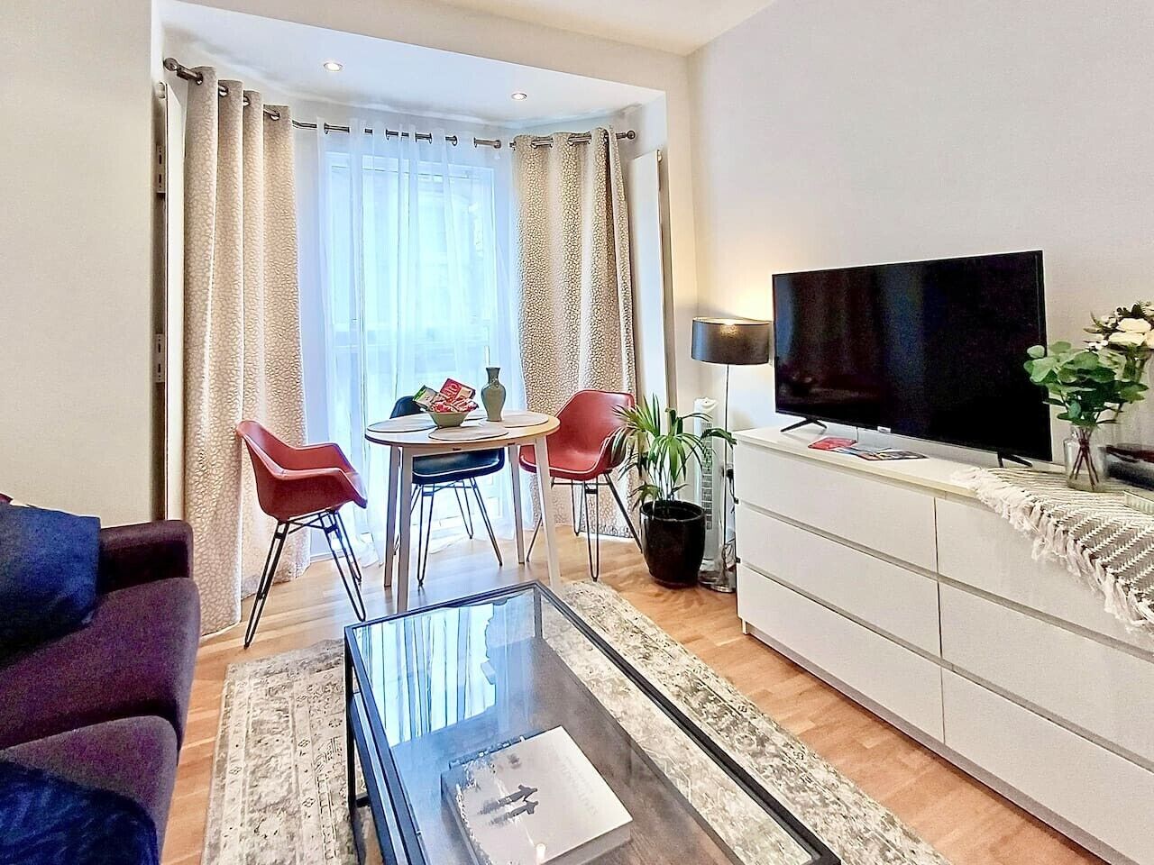 Ein Wohnzimmer mit Flachbildfernseher, einem Glastisch, einer Essecke mit Stühlen und einer Couch.