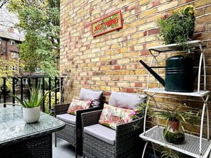 An outdoor seating area with wicker chairs and a table, a brick wall, and a sign that reads 'JUST VIBING'.
