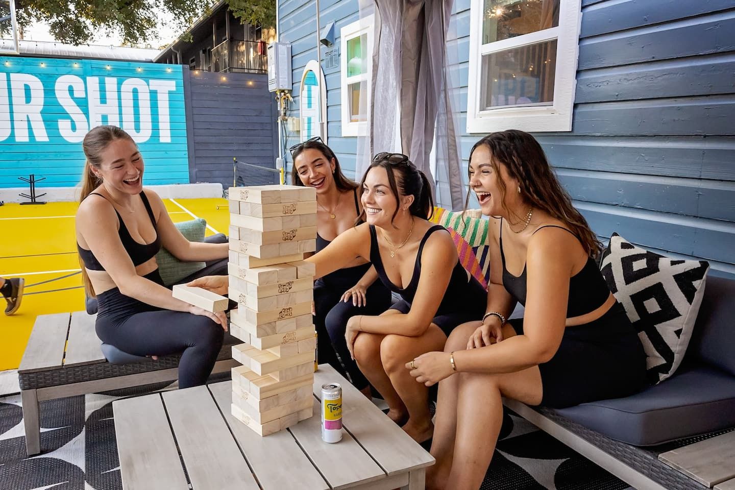 Four people playing a board game outdoors with a can of beer on a table.