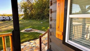 A stone pathway leading to a wooden deck with a fire pit, surrounded by a grassy yard and trees. - New Cabin for an Adventure (Peculiar)