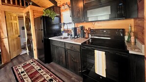 A kitchen with wooden cabinets, a black refrigerator, a microwave, and a stove. - New Cabin for an Adventure (Peculiar)
