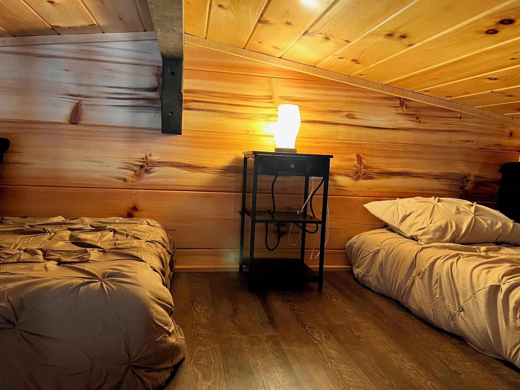 Een kamer in chaletstijl met twee bedden, een houten plafond en een tafellamp.