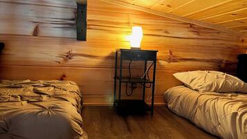Een kamer in chaletstijl met twee bedden, een houten plafond en een tafellamp.