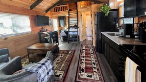 A cozy cabin interior with a wooden ceiling, a dining area, a kitchen, and a living room with a sofa and a coffee table. - New Cabin for an Adventure (Peculiar)
