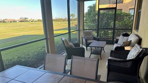 A covered patio area with a view of a golf course, furnished with wicker chairs and a table.