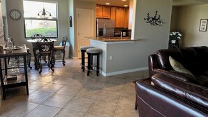 A spacious living area with a leather couch, a dining table with chairs, and a kitchen area with wooden cabinets and a refrigerator.