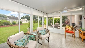 A sunroom with wicker furniture, a dining area, and large windows offering a view of the garden and neighboring houses. - 3-bed house in fabulous Fort Myers with WiFi, AC,   6 miles from the Airport.   (Fort Myers)