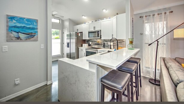 A modern kitchen with white cabinets, stainless steel appliances, and a marble island with bar stools. - 3-bed house in fabulous Fort Myers with WiFi, AC,   6 miles from the Airport.   (Fort Myers)