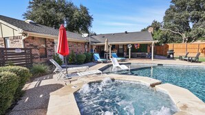 A backyard with a hot tub, lounge chairs, and a covered patio area. - Resort Pool & Spa Retreat with Game Room, Patio, Foosball & BBQ (North Richland Hills)